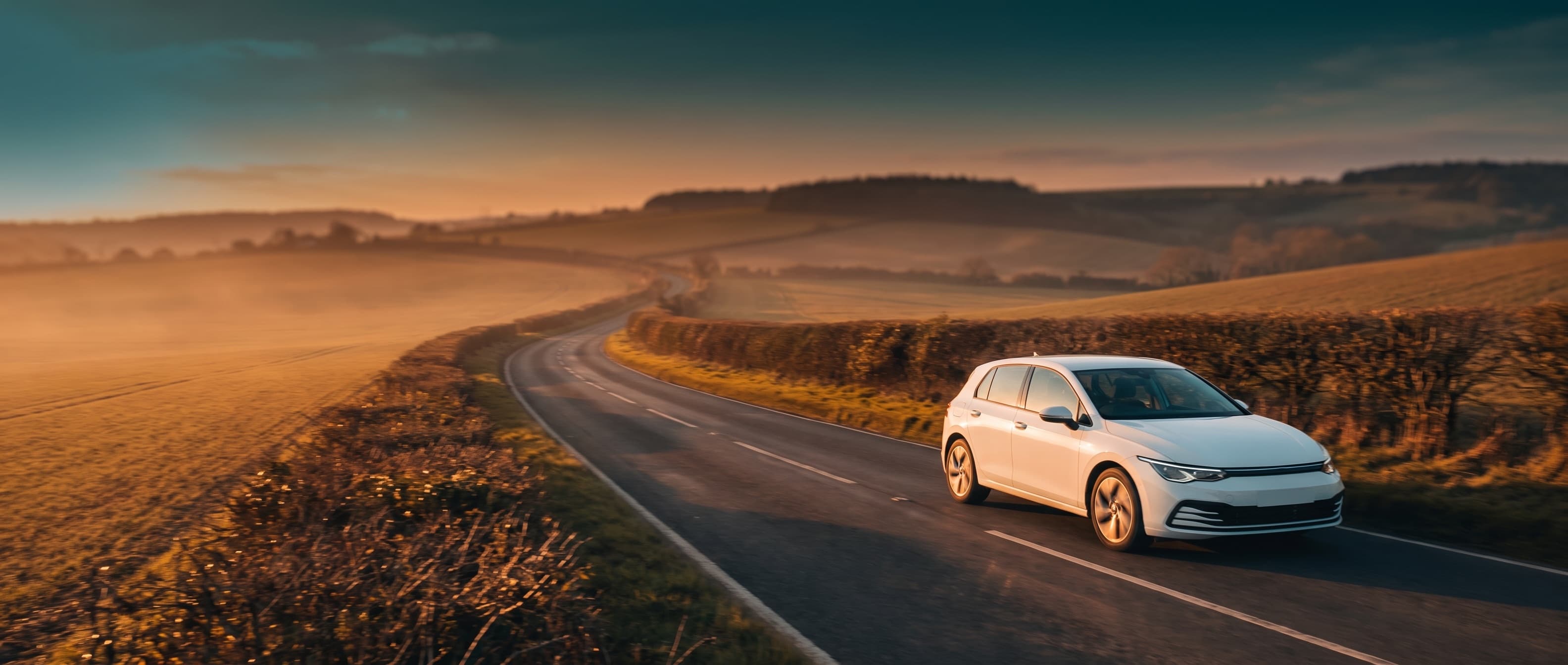 White hatchback on a winding Surrey country road at golden hour